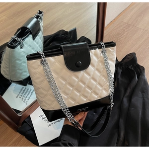 Close-up of quilted black and white bucket bag with silver chain strap on wood floor