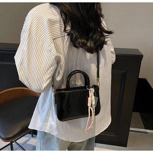 Detail of a black patent leather handbag with pink braided charm on a striped shirt