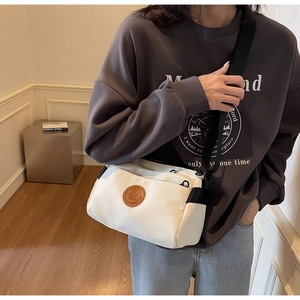 Détail d'un sac bandoulière crème minimaliste avec un patch logo en cuir marron rond