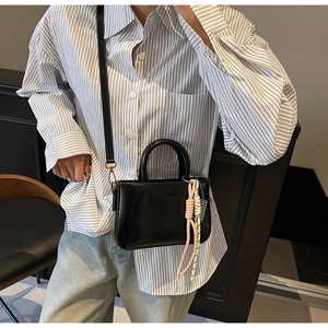 Detail of a black glossy leather crossbody bag with decorative rope charms and shoulder strap