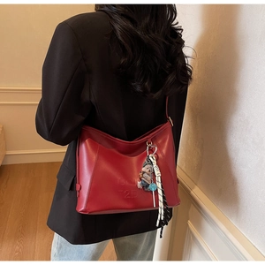 Detail of red leather underarm bag with side pleats and pendant on a black blazer