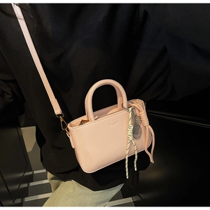 Close-up of a light pink small square bag featuring a top handle and gold metal hardware