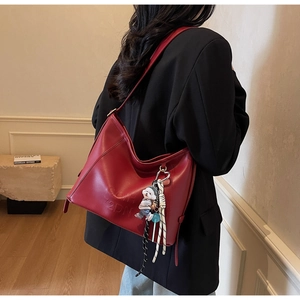 Detail of burgundy shoulder bag with embossed letters and a cute character pendant