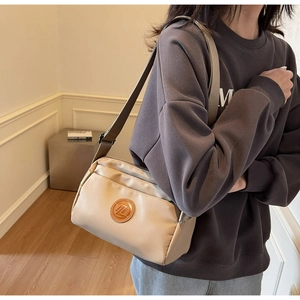 Détail d'un sac bandoulière en nylon crème avec logo en cuir marron et sangle tissée