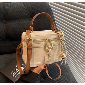Détail du sac boîte vintage crème avec poignée en cuir marron et breloque à pompon