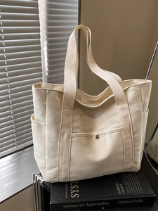 Minimalist cream canvas tote bag with multiple pockets on a stylish metal shelf