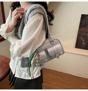 Detail of light gray glossy shoulder bag with double buckled pockets and cute bear charm
