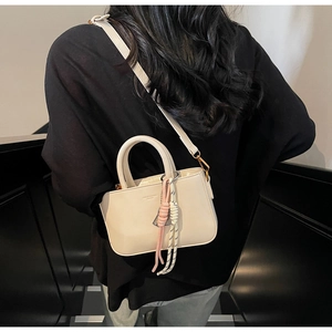 Detail of off-white PU leather square handbag with braided charms shown on a model