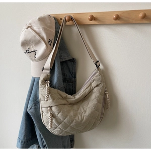 Detail of beige quilted dumpling bag with adjustable strap and braided knot zipper pull
