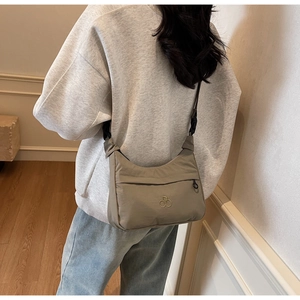 Vista laterale di una borsa a tracolla in nylon kaki chiaro con logo metallico