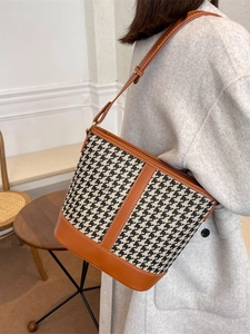Sac seau chic motif pied-de-poule avec bordure en cuir marron porté à l'épaule ici