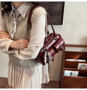 Detail of dark red glossy leather shoulder bag with pockets and bear charm accessory