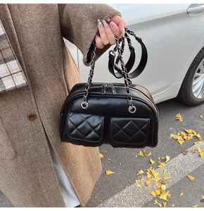 Detail of a black quilted leather pillow bag with silver chain straps in an autumn setting