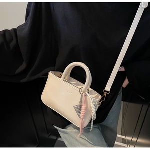 Close-up of cream square handbag featuring logo detail and braided decorative charm