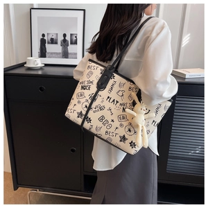 Detail of a beige tote bag featuring black graffiti art prints and a cute plush bunny charm