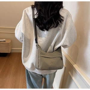 Dettaglio della borsa a tracolla in nylon grigio con logo indossata dal modello