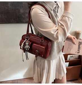 Detail of burgundy underarm bag with double pockets and bear charm worn by a model