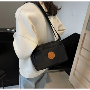 Détail de la sacoche noire en nylon avec logo en cuir marron et bandoulière réglable
