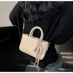 Detail of a minimalist cream PU leather handbag with woven rope charm and dual handles