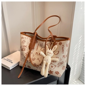 Detail of a beige tote bag with brown graffiti patterns and a cute rabbit pendant