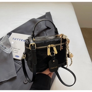 Détail du sac boîte noir avec fermetures dorées, étiquette en cuir et breloques élégantes