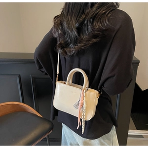Detail of cream-colored rectangular handbag with fashion text and woven rope charm