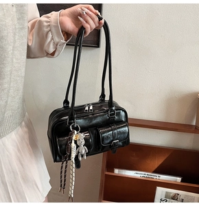 Detail of black faux leather shoulder bag with twin front pockets and a silver bear charm