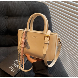 Detail of cream mini handbag with woven rope charm and adjustable strap held in hand