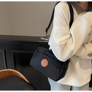 Détail d'un sac bandoulière noir montrant sa texture en nylon et son logo rond en cuir