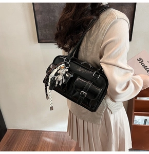 Close-up of black patent leather Boston bag featuring buckle pockets and bear charm