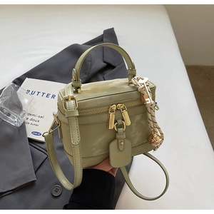 Détail du sac boîte vert pistache avec zips dorés, poignée supérieure et breloque clochette