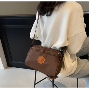 Gros plan d'un sac bandoulière en nylon marron porté montrant texture et détails zippés