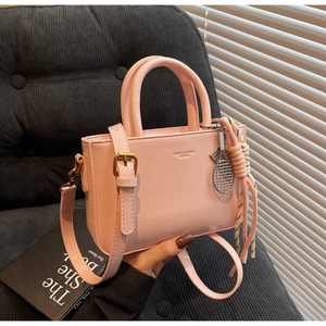 Detail of light pink leather handbag featuring a white woven charm and brand engraving