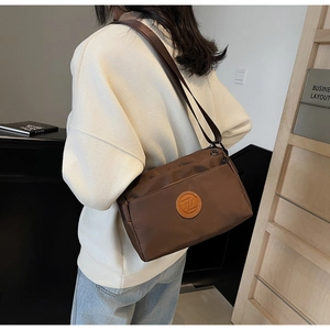 Sac bandoulière en nylon marron porté à l'épaule avec une large sangle tissée confortable