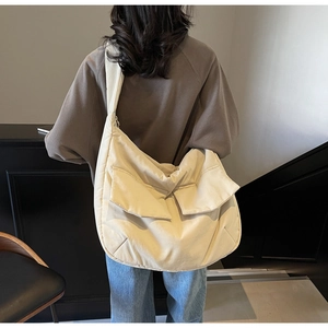 Large beige canvas tote bag with front pockets shown on shoulder for a stylish urban look