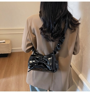 Glossy black patent leather shoulder bag with bow and ruched strap on model