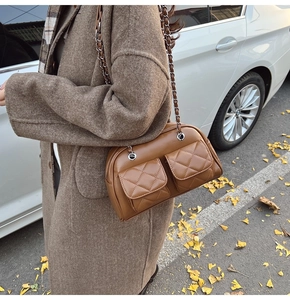 Close-up of caramel leather quilted crossbody bag with silver chain strap in autumn street setting