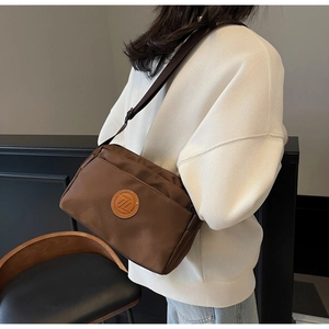 Détail du sac bandoulière en nylon marron avec logo en cuir et bandoulière en tissu marron