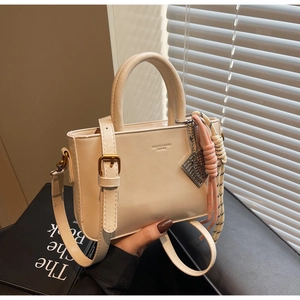 Detail of cream leather handbag showing top handle and adjustable shoulder strap attachment