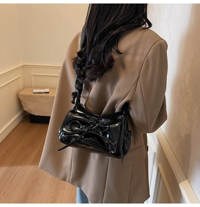 Detailed view of black glossy shoulder bag with oversized bow and wide strap on model