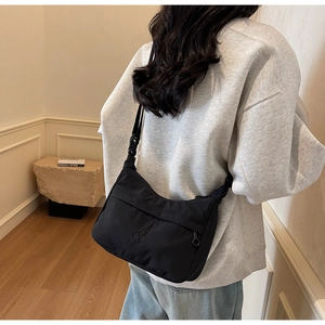 Dettaglio della borsa a mezzaluna in nylon nero con logo ricamato e tracolla