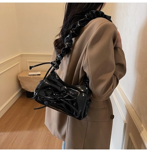 Detail of black patent leather shoulder bag with bow and ruched cloud strap design