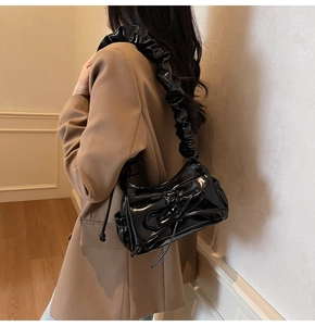 Close-up of black glossy patent leather shoulder bag featuring a large bow and pleated strap