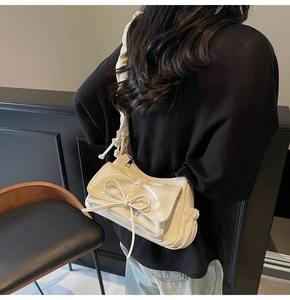 Detail of white glossy shoulder bag with bow decoration and pleated strap texture