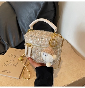 Detailed shot of tweed box bag with golden chain strap and plush ball charm