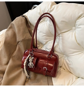 Detail of burgundy patent leather shoulder bag featuring dual front pockets and bear charm