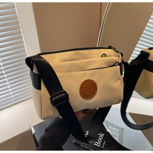Détail du sac bandoulière en nylon crème avec poches zippées et écusson logo en cuir brun