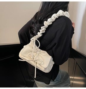 Side view of cream-white bow shoulder bag with ruched cloud-style strap on a model