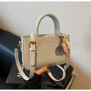 Detail of minimalist beige leather handbag featuring logo debossing and tennis charm