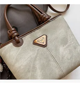 Detail of grey fabric tote with brown leather trim and triangle metal logo plaque